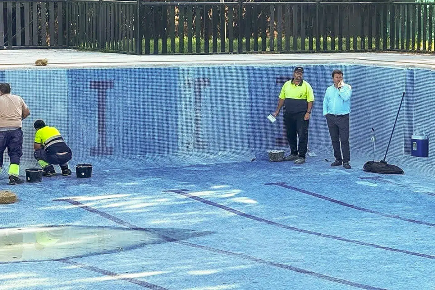 Operarios municipales realizando labores de limpieza en el vaso principal de la piscina municipal de Santa Olalla antes de la apertura